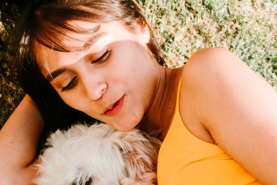 A person lying in the grass beside a small white dog.